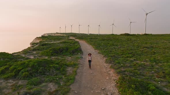 Attractive girl traveling with a backpack walking on the road near the windmill farm alt
