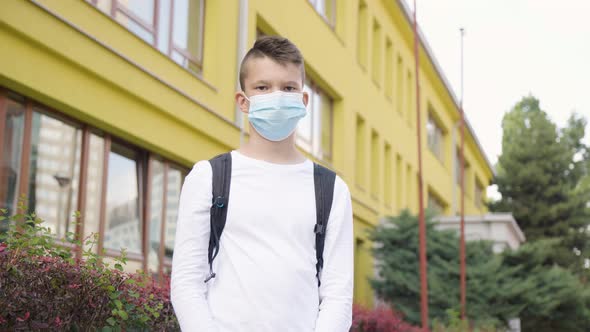 A Caucasian Teenage Boy in a Face Mask Shows a Thumb Up to the Camera and Nods  a School