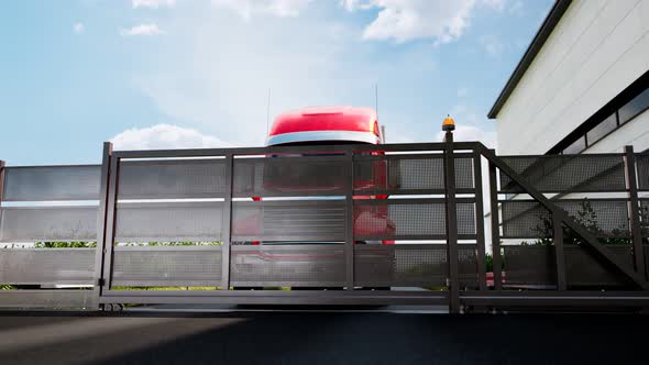 Red truck with heavy cargo. The gate opens and a giant lorry leaves the parking. alt