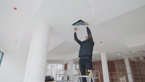 Master Stands on a Ladder in the Room Without Repair and Repairs the Air Conditioner alt