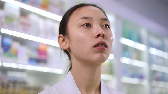 Headshot Portrait of Intelligent Asian Young Beautiful Woman Choosing Pills on Shelves in Pharmacy alt