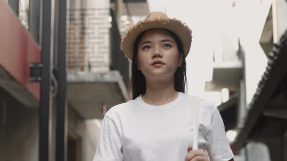 Attractive beautiful Asian female walking and looking around a small street enjoying vacation. alt
