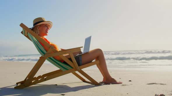 Woman with hat using laptop at beach in the sunshine 