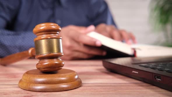 a Gavel on Table with Young Man Reading a Book on Background alt