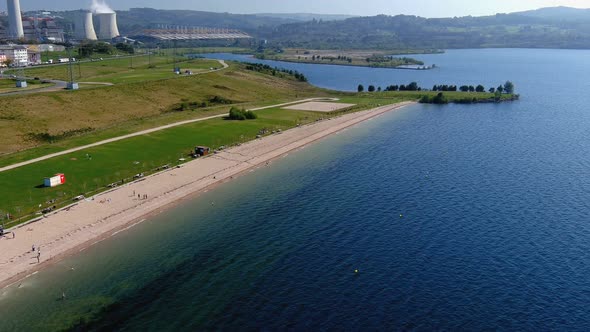 people enjoying the lake beach thermal power plant with gardens and clean water on a sunny afternoon alt