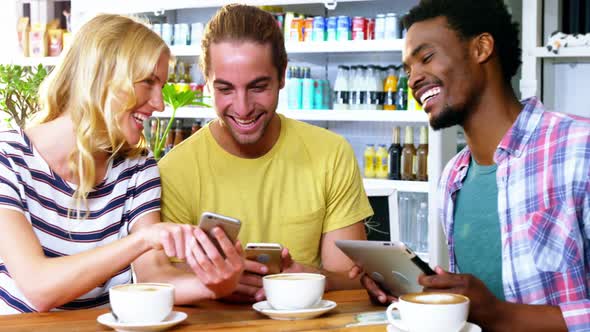 Three friends using mobile phones while having cup of coffee alt