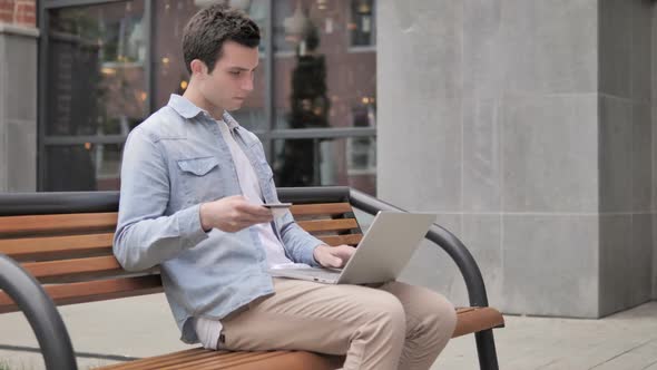Online Shopping By Young Man Sitting on Bench alt