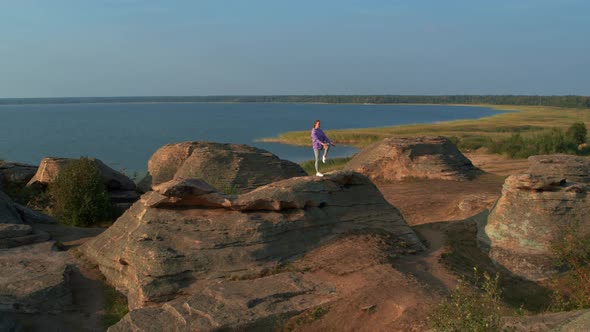 A Girl is Doing Fitness on a Hill on the Lake Shore