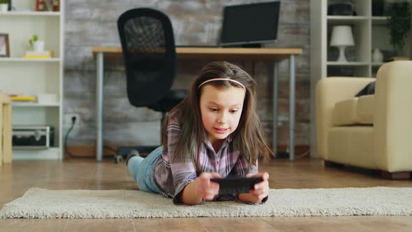 Cheerful Little Girl Lying Down on the Floor Playing Video Games alt