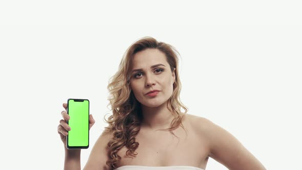 Distressed Woman Points Finger at Green Screen of Smartphone alt