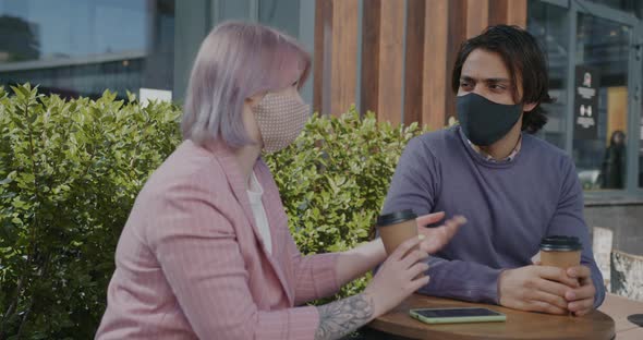 Portrait of Man and Woman Wearing Masks Talking at Table in Cafe During Pandemic alt