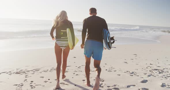 Caucasian couple holding surfboards on the beach alt