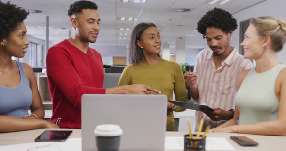 Happy diverse male and female business colleagues talking and using laptop in office alt