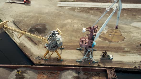 Large Harbor Cranes Onshore at the Quay Unload a River Gravel Barge Onto a Large Pile alt