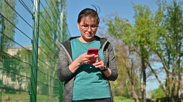 Active Mature Woman in Sportswear with Smartphone Outdoor alt