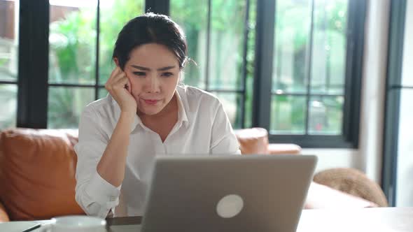 Portrait of Asian businesswoman sitting on table and feeling boring working on computer at home. alt