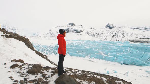 Young Woman Tourist in a Red Jacket Walks Around Huge Glacier in Iceland alt