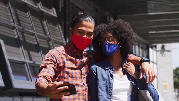 Diverse colleagues wearing face masks taking selfie using a smartphone alt