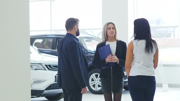 Young Couple Buying New Car in Dealership and Talking To Helpful Manager in Suit