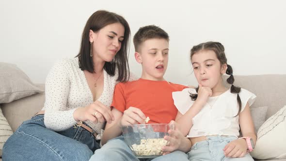 Mom and Children Eat Popcorn Sitting on the Couch They Laugh and Enjoy Life alt