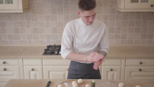 Young Pizza Maker in Cook Uniform Rolling Dough Balls for Pizza in the Kitchen. Food Preparation alt