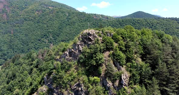 Summit Cross At The Rocky Cliff And Green Forest Covered The Mountain Range. aerial alt