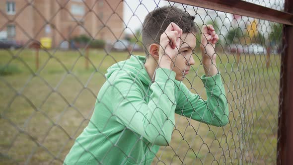 Refugee Serious Boy Stands Alone Head Bowed Near the Fence Regrets Actions alt