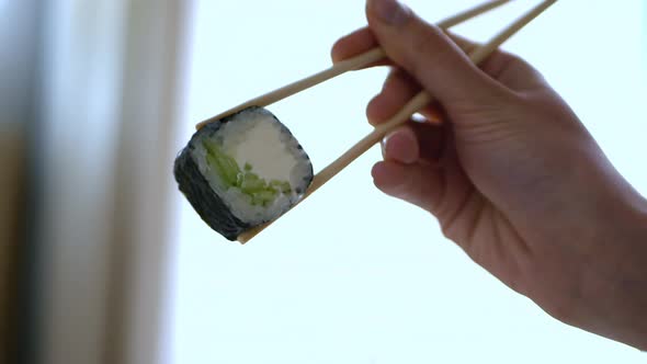 A Woman's Hand Dips Futomaki with Cucumber in Soy Sauce