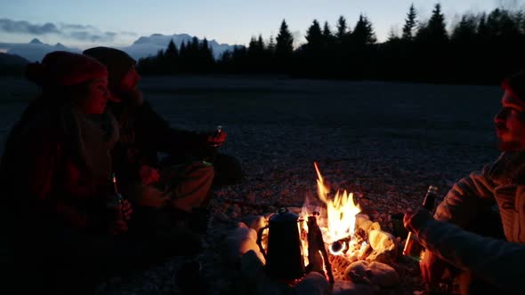 Group of friends sitting at a bonfire at dawn alt