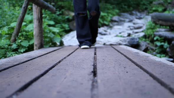 Cinematic  girl in wide dark pants crosses a river on a wooden bridge in the woods in slow motion