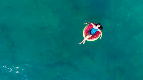 A Woman Is Floating Along the Sea in a Rubber Ring in a Top View alt