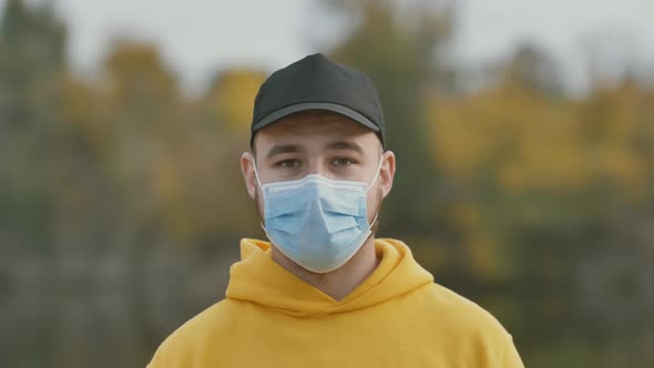 Portrait of a Young Man Putting on a Protective Medical Mask on the Street