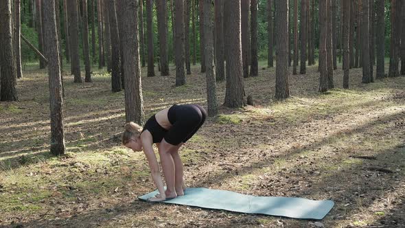 Flexible Fit Female Practices Yoga Performs Surya Namaskar at Sunny Pine Forest alt