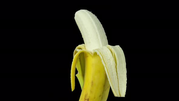 Animated Footage of a Half Peeled Banana Turning Against Black Background alt