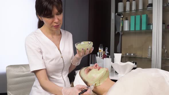 The Cosmetologist Cleanses the Face with a Green Clay Mask