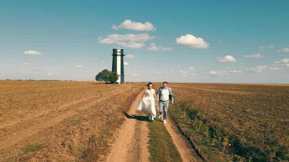 Two Happy Young People Running Together Holding Hands in a Field alt