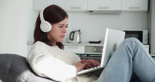 Programmer Woman in Headphone Lying in Cozy Couch Typing Code at Home alt