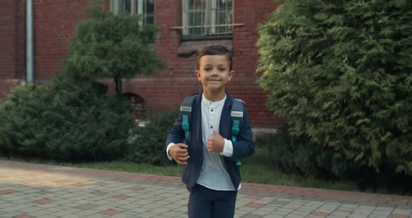 Crop View of Happy Little Boy Running and Looking To Camera. Child in School Uniform with Backpack alt