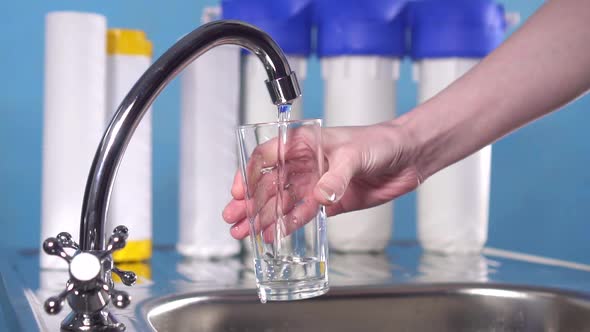 Hand Pours Clean Drinking Water From Under the Filter on a Blue Background alt