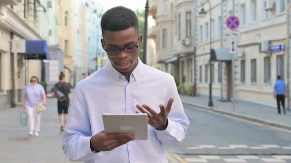 African Man Making Video Call on Tablet While Walking on the Street alt