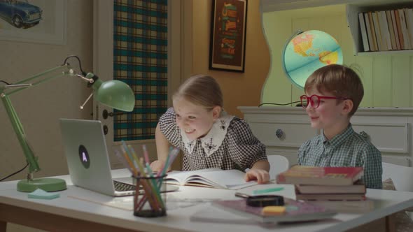 Two Siblings Have Online Lesson Sitting at Desk at Home