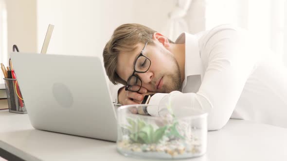 Tired Businessman Sleeping on Table Near Laptop After Working Night in Startup.