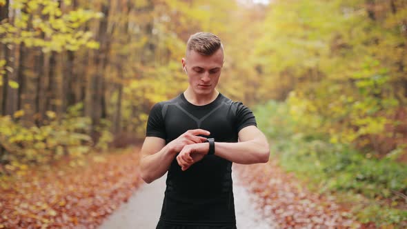 The Athlete is Starting Training on the Watch and Turning on Music in Headphones alt