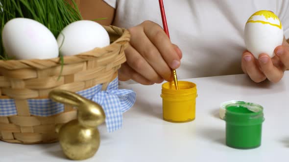 A young child prepares for the religious holiday of Easter by painting eggs with paint.