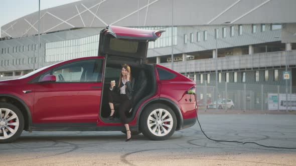 Handsome Girl Sitting in Side Auto with Opened Door and Talking on the Phone alt