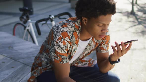 African american man in city, sitting on step drinking coffee and using smartphone in the street alt