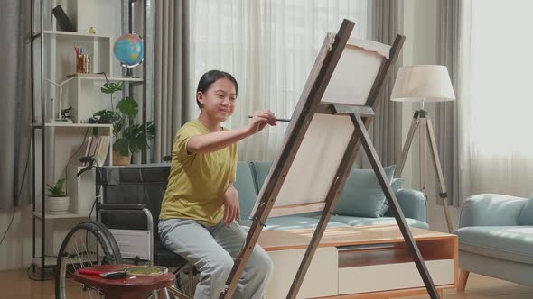 Asian Artist Girl In Wheelchair Holding Paintbrush Mixed Color And Painting On The Canvas alt