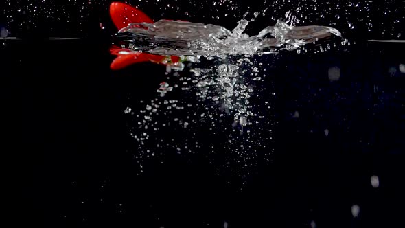 Colorful red sweet pepper being dropped into water in slow motion. alt
