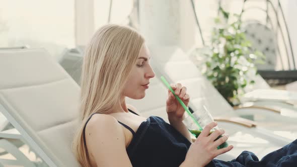 Medium Shot of Blonde Young Woman Drinking Cooling Mint Drink From a Straw