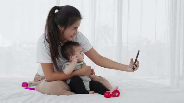 Asian mother watching the smartphone with her baby on the bed